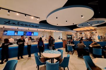 Interno del Banco di Cannavacciuolo a Malpensa. Arredamento blu, tavoli e persone. Antonino Cannavacciuolo, chef stellato.