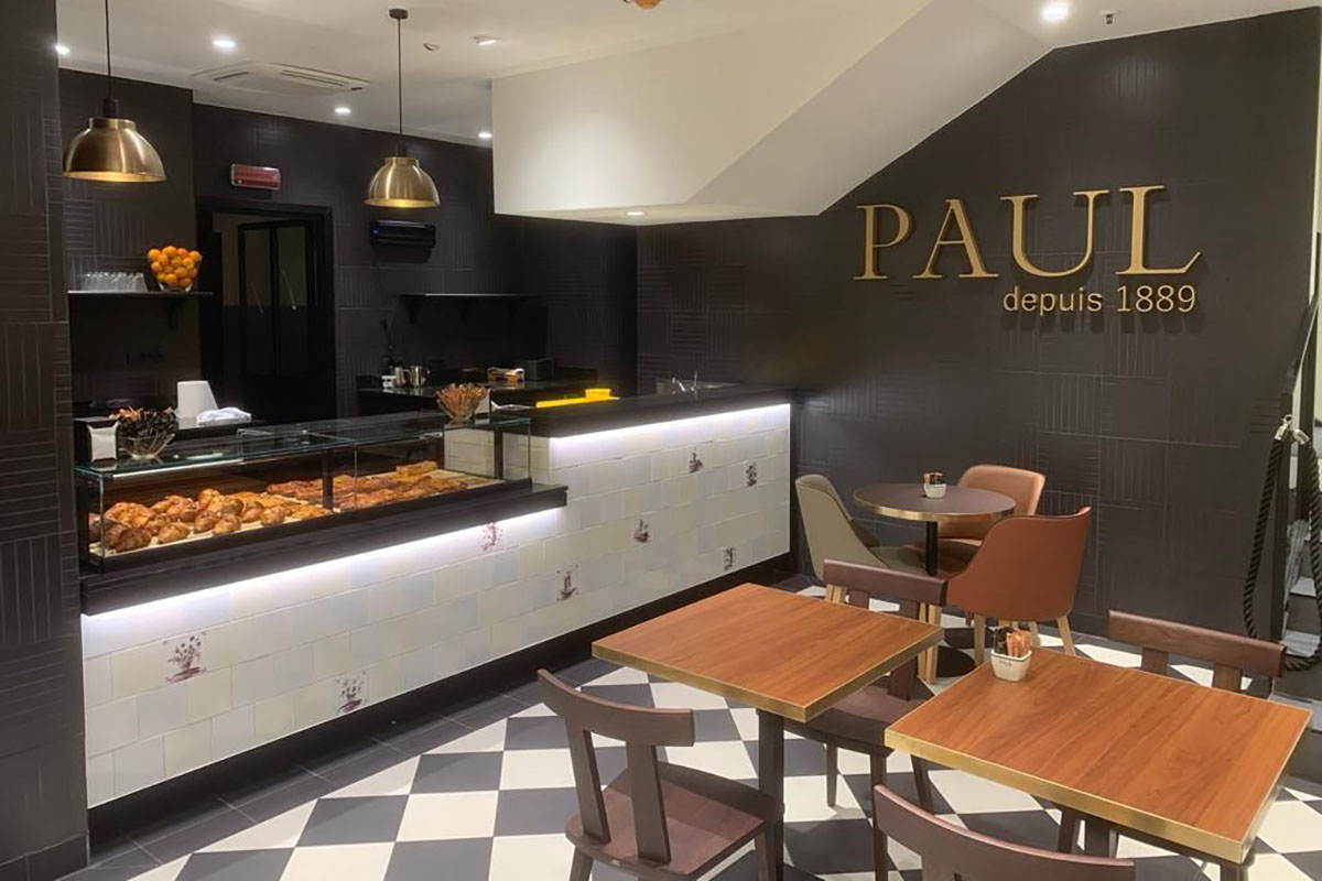 Interni della bakery francese Paul a Milano Centrale con vetrina dolci e tavolini.