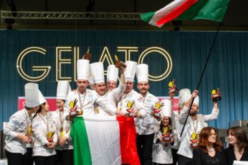 Team Italia vincitore Gelato World Cup 2024! Podio con chef, bandiera italiana e trofei. Trionfo gelato artigianale.