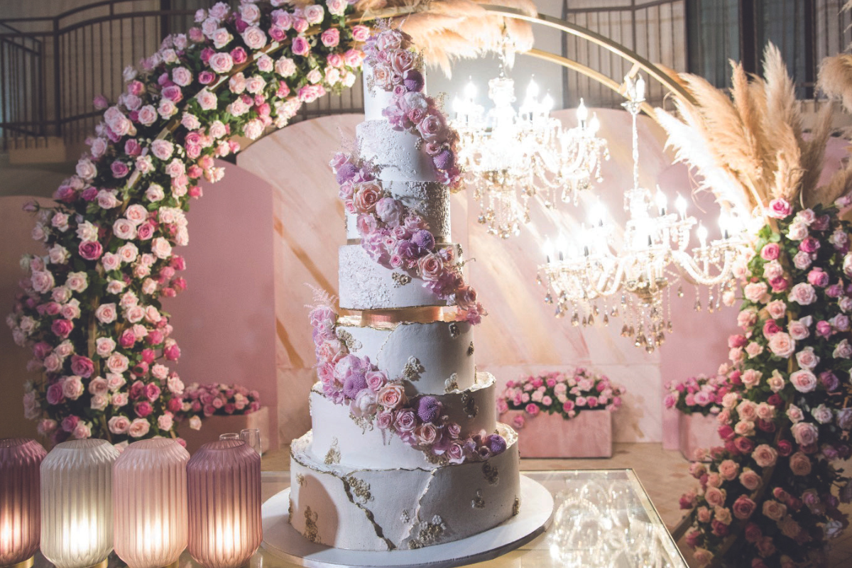 Elegante torta Chiffon a piani decorata con fiori rosa, lampadari e arco floreale.