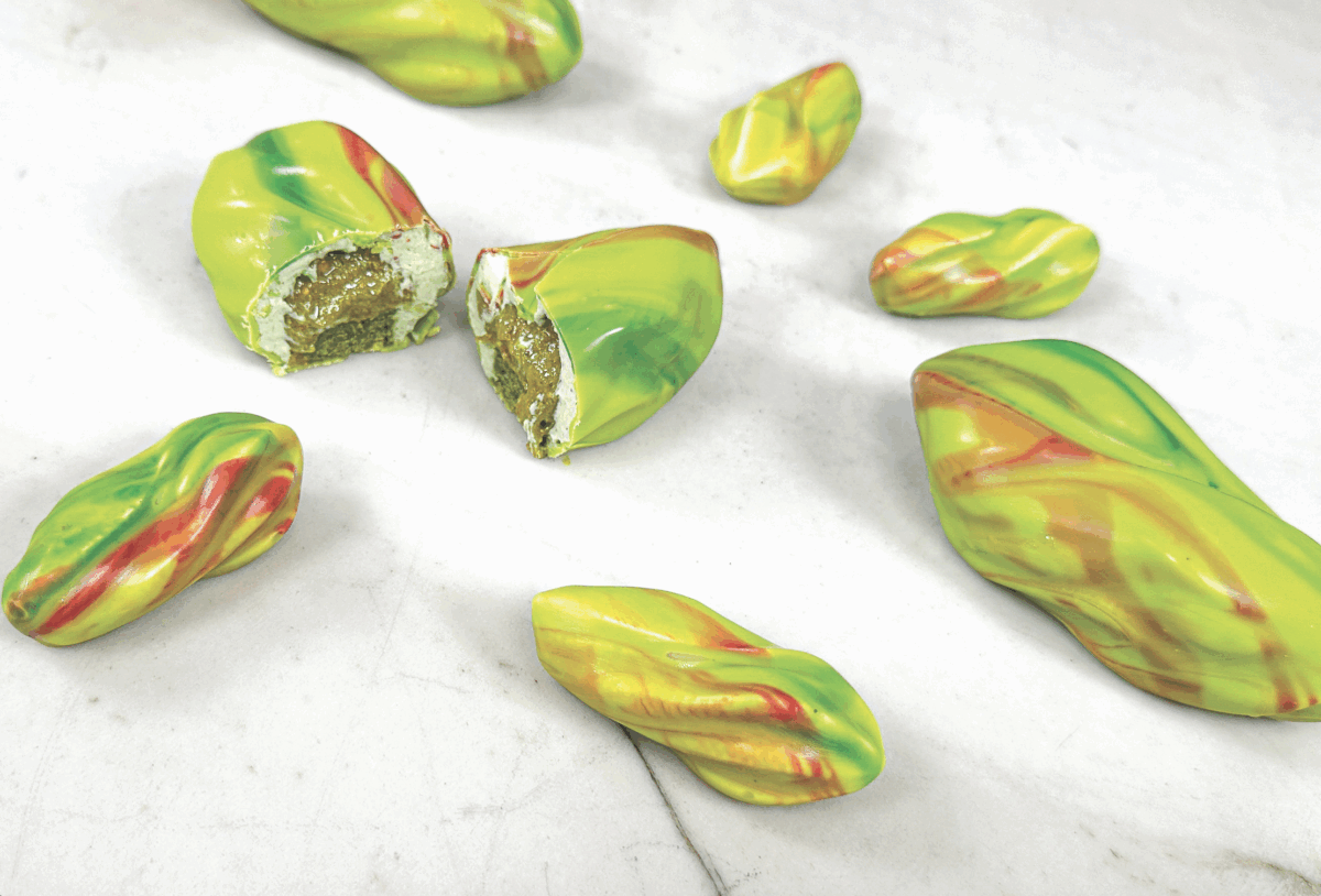 Dolci pistacchio trompe-l'œil. Pasticceria creativa, cioccolatini a forma di pistacchio con ripieno. Delizie al pistacchio.